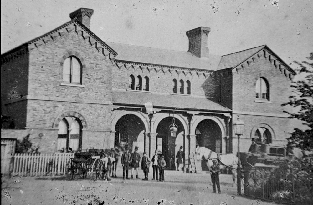 A black and white photo of Horsham railway station with horse and carts outside