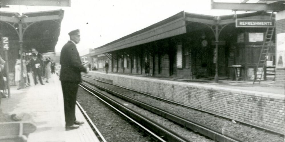 A black and white photo of a Horsham station platform. A guard in uniform stands in the foreground