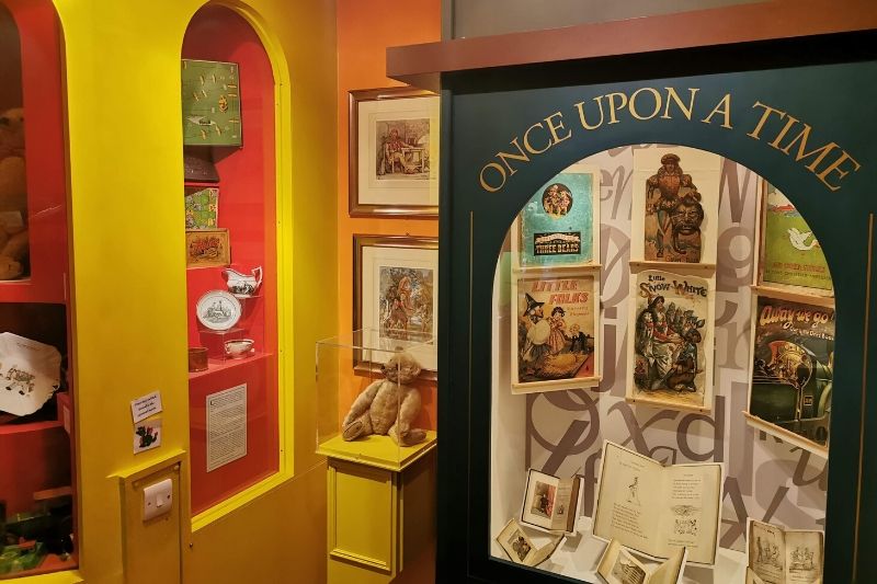 A cabinet with the words Once upon a time contains story books. The yellow and red walls display toys from different eras