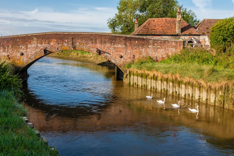 A red-brick bridge over the River Adur. Swans swim on the water.