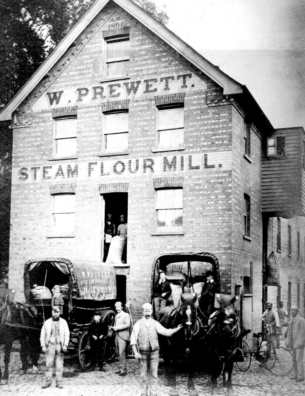 Four-storey brick-built steam flour mill. There are two horse-drawn wagons at the front, and a number of men and boys (presumably workers)