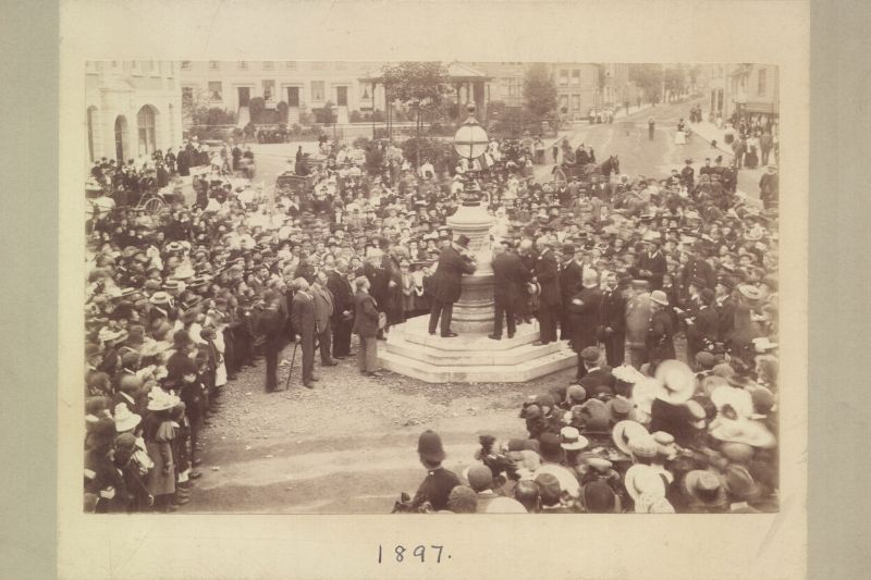 A black and white photo of crowds around Horsham town centre water fountain dated 1897