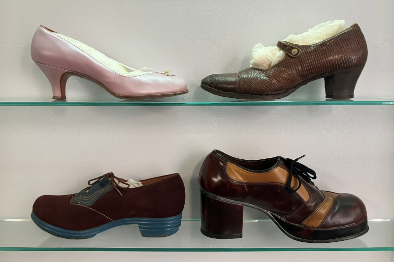 Photograph of 4 antique shoes spread across two glass shelves